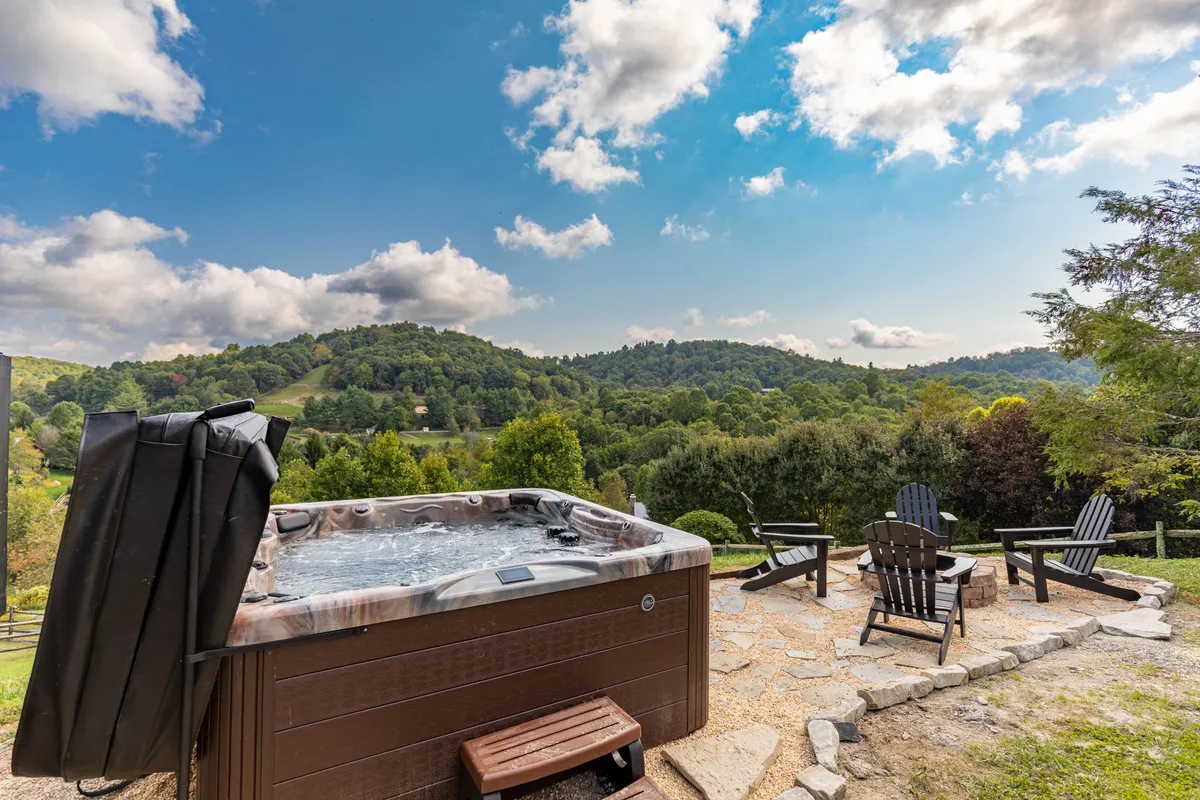 A tranquil setting with a bubbling hot tub and Adirondack chairs overlooking a sweeping mountain view. The space is perfect for unwinding and taking in sunsets or stargazing.