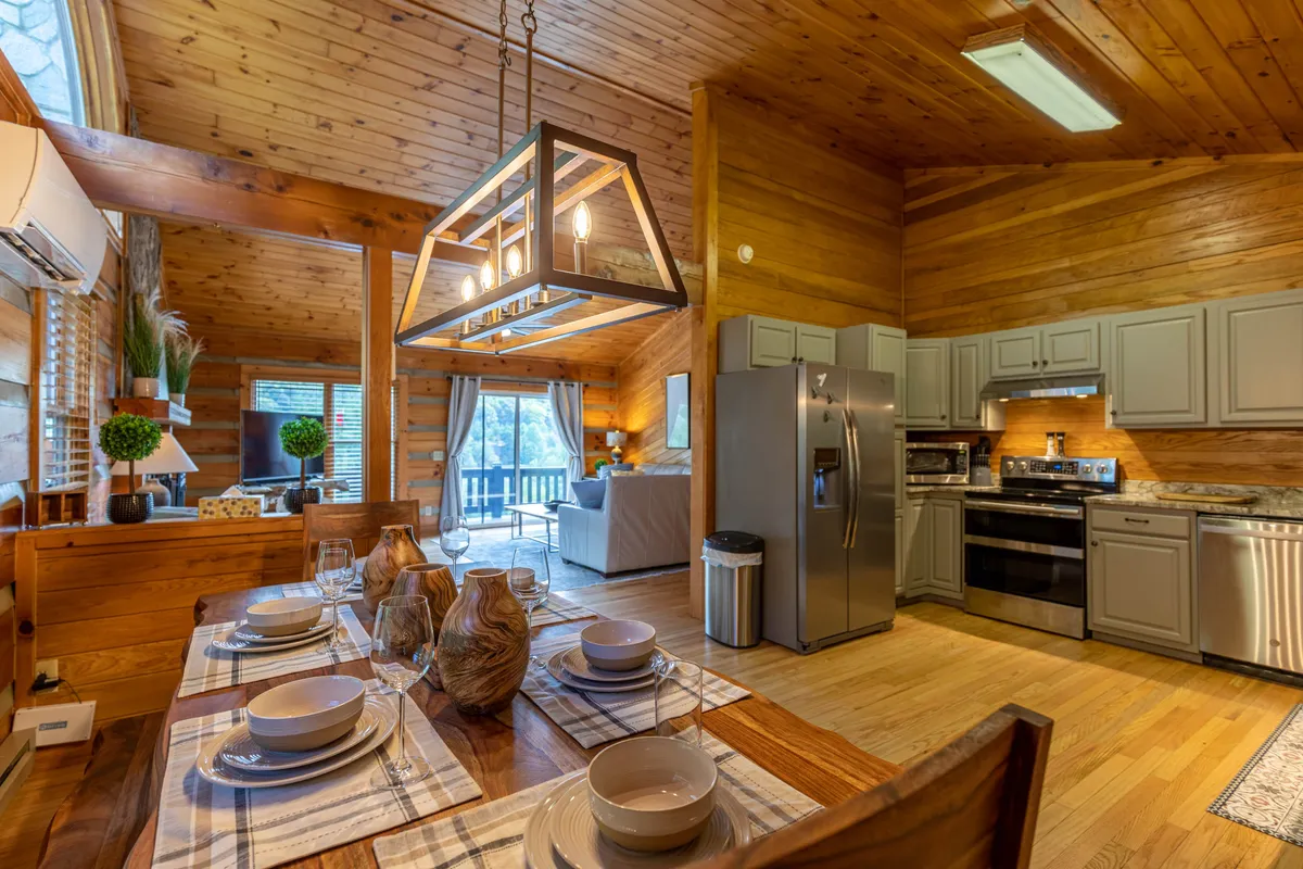 A spacious, stylish dining area with a large table set for a meal, modern pendant lighting, and an open view to the kitchen and adjacent seating. The scene is ready for family dinners or festive gatherings, seamlessly connecting cooking and dining experiences.