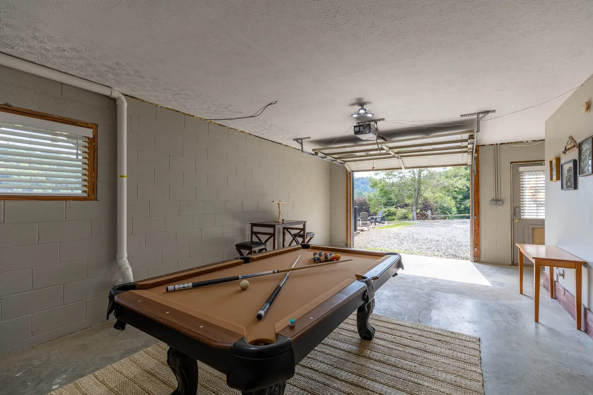 A converted garage game room with a pool table positioned centrally. There is a seating area along the wall, the garage door is visible, and the space is bright and inviting, ideal for group games and friendly competition.