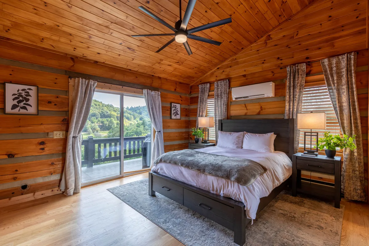 A tranquil bedroom with a plush bed facing a large window that lets in ample natural light. Plants, nightstands, and tasteful artwork create a restful and inviting atmosphere. The cozy linens and soft textures reinforce a feeling of comfort and relaxation, ideal for restful nights after a day of adventure.