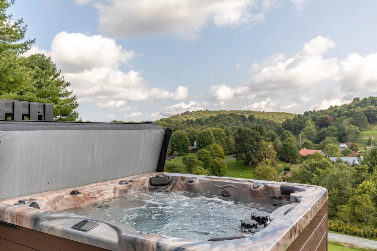 This exterior image features a hot tub set against a backdrop of distant hills and trees, inviting guests to relax while enjoying the surrounding natural beauty. The scene evokes moments of relaxation, group conversation, and stargazing under the open sky.