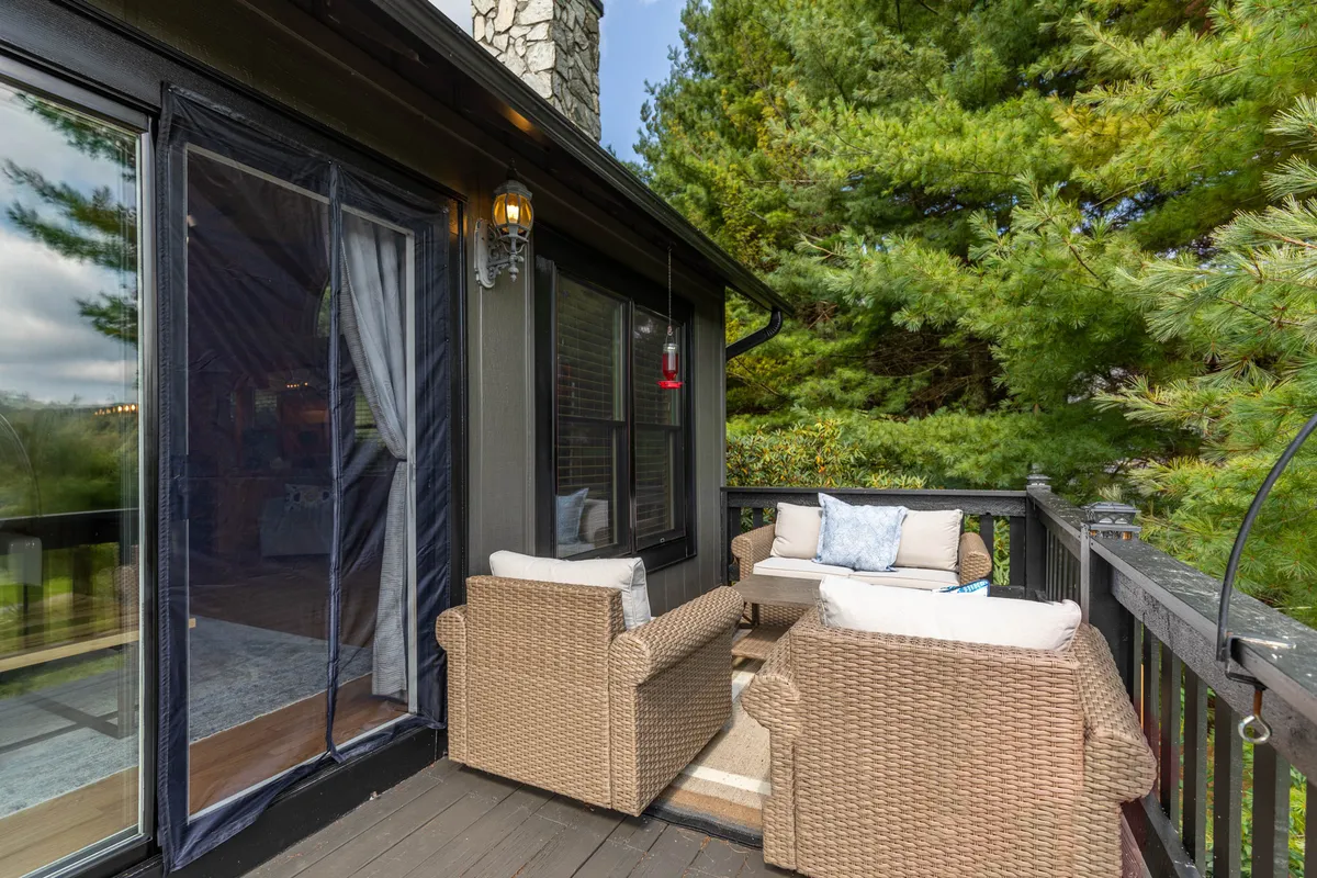 An inviting outdoor seating area featuring wicker chairs and a cushioned sofa, surrounded by lush greenery. The setup suggests a comfortable spot for relaxing, reading, or casual conversations, all while enjoying the natural beauty around the lodge.