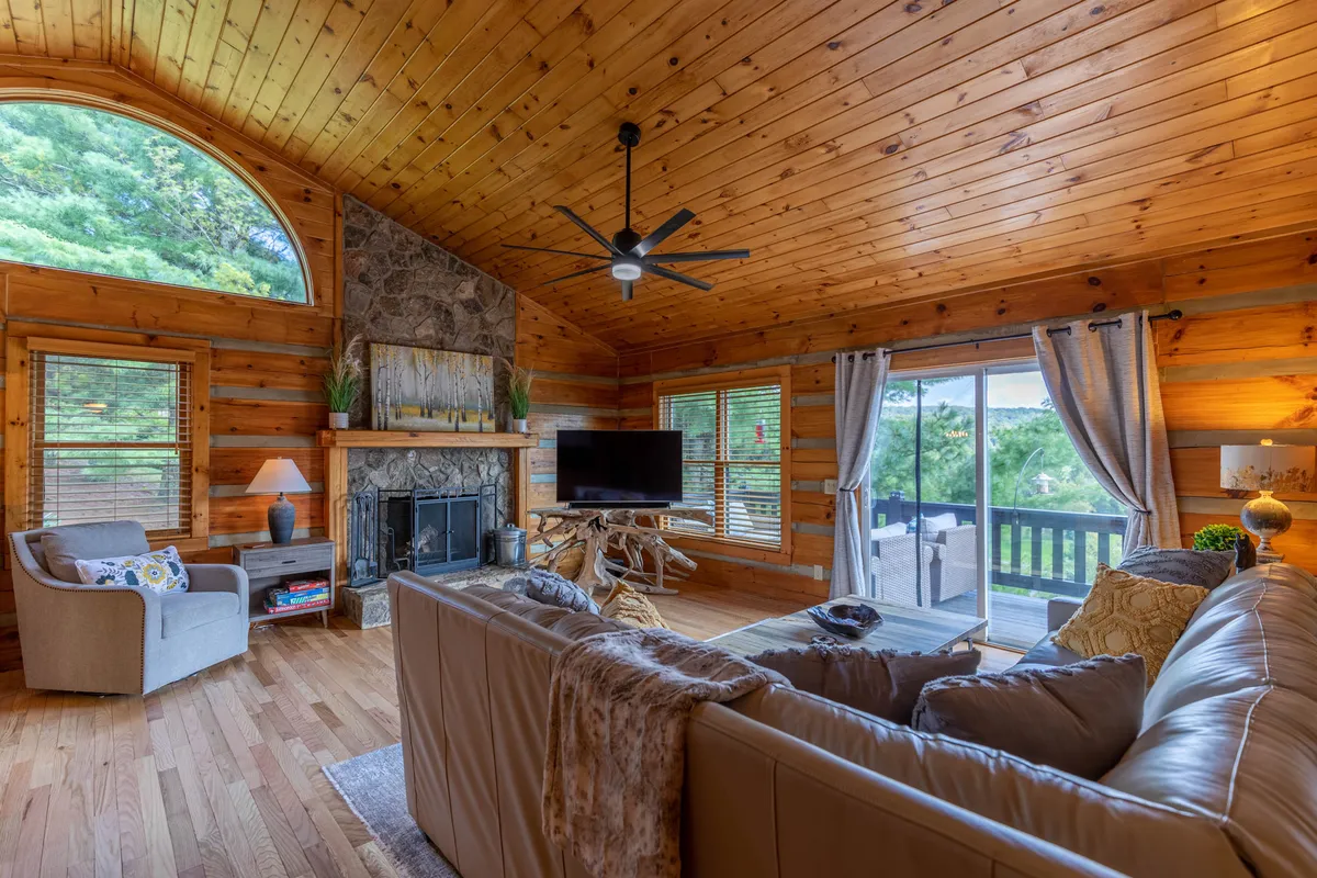 A comfortable great room with a large stone fireplace as a stunning focal point, plush seating, a smart TV, and expansive windows offering natural light and scenic views. The space invites relaxation, family movie nights, and cozy evenings by the fire.