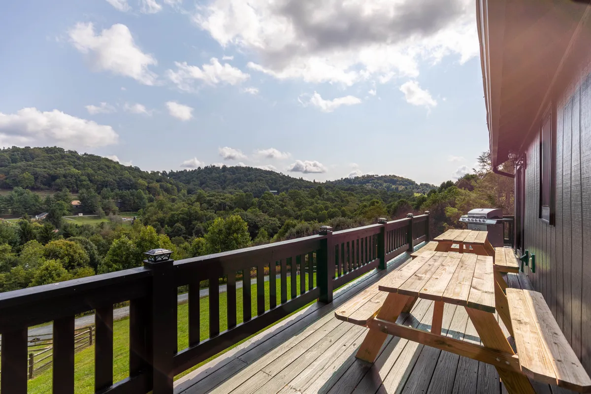 A serene deck scene with sturdy wooden picnic tables positioned to take advantage of mountain and sky views, framed by greenery and a peaceful atmosphere.