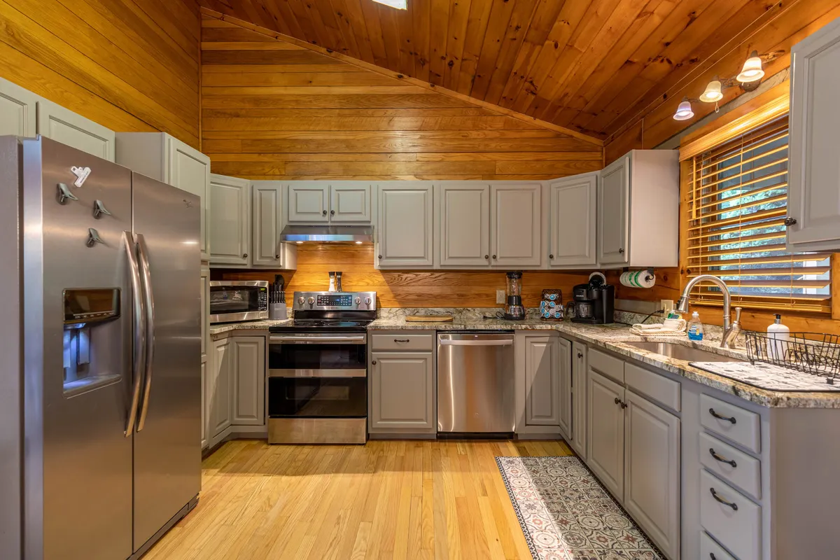 A sunlit, open kitchen featuring gleaming granite countertops, stainless steel appliances, and warm wooden cabinets. Natural light pours in from multiple windows, enhancing the inviting, homey atmosphere. The layout offers plenty of space for meal prep and easy movement, making it ideal for social cooking and family gatherings.