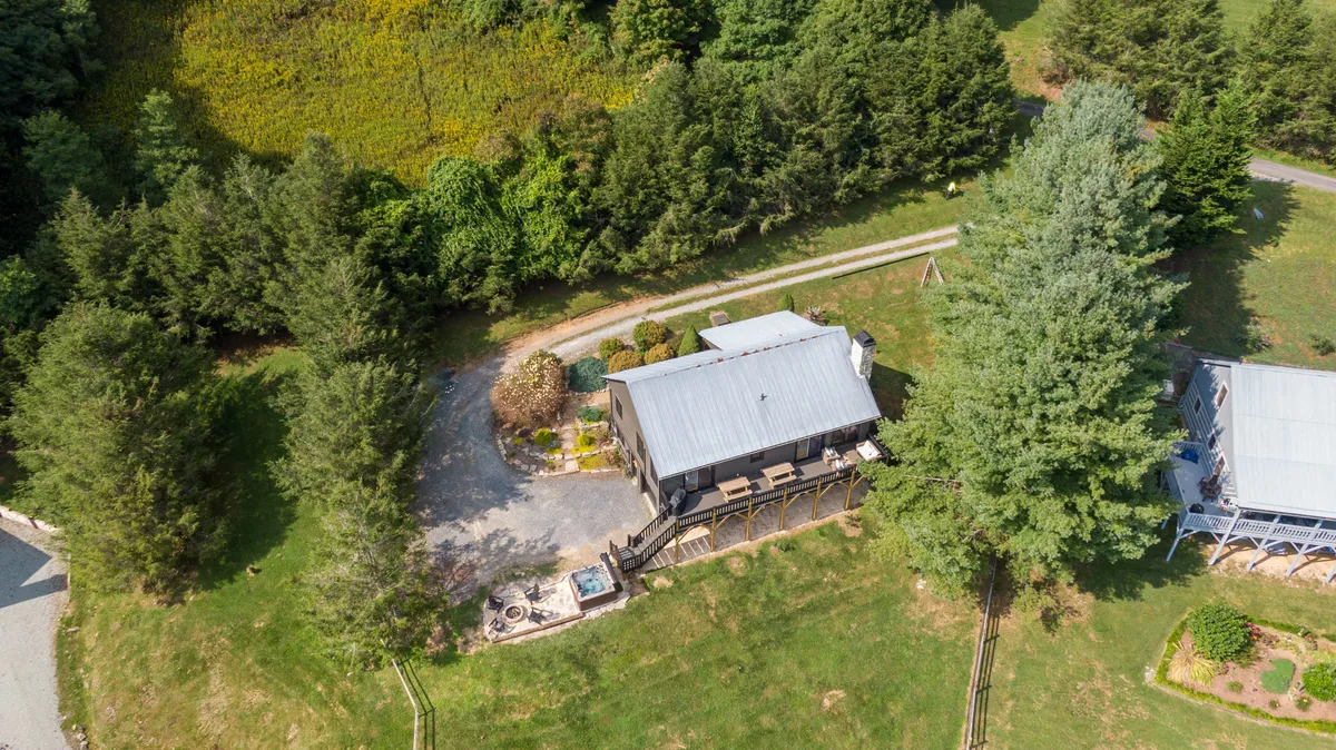 This exterior image captures the main house, a spacious deck area, a welcoming fire pit, and abundant greenery surrounding the property. The scene suggests opportunities for families to gather outdoors, play in the yard, or relax together after a day of adventure.
