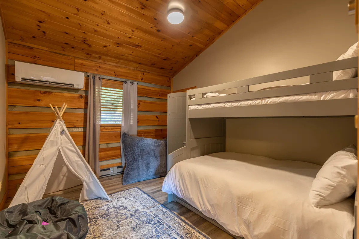 A whimsical bunk room featuring a sturdy twin-over-full bunk bed with white bedding, a playful teepee tent, and a soft area rug. The design is child-friendly, inviting imaginative play and cozy sleepovers for families with children.